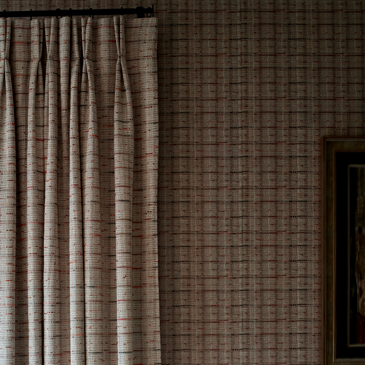 A close-up of a pleated curtain panel hanging on a dark rod against a matching patterned wallpaper with a subtle grid design.